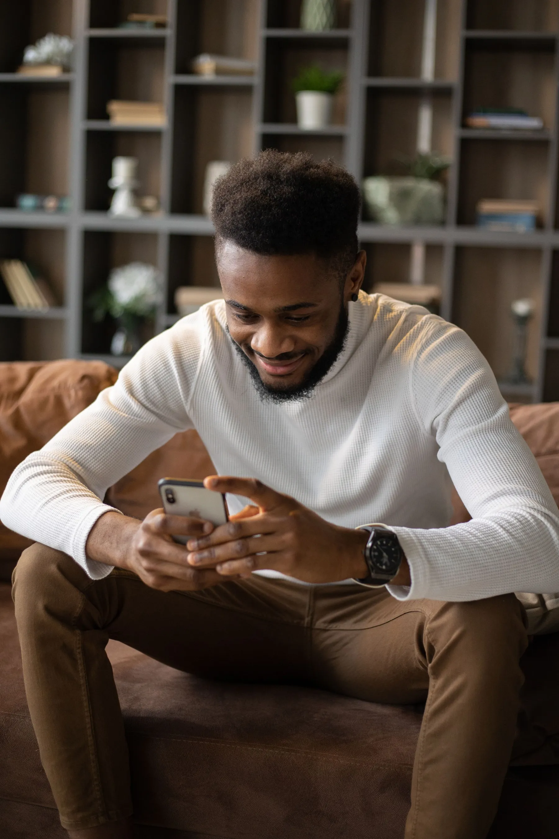 A man on his sofa at home, smiling as he reads an update from his mother's day center on his phone